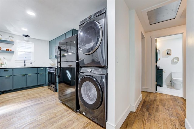 laundry area with sink, light hardwood / wood-style floors, and stacked washing maching and dryer