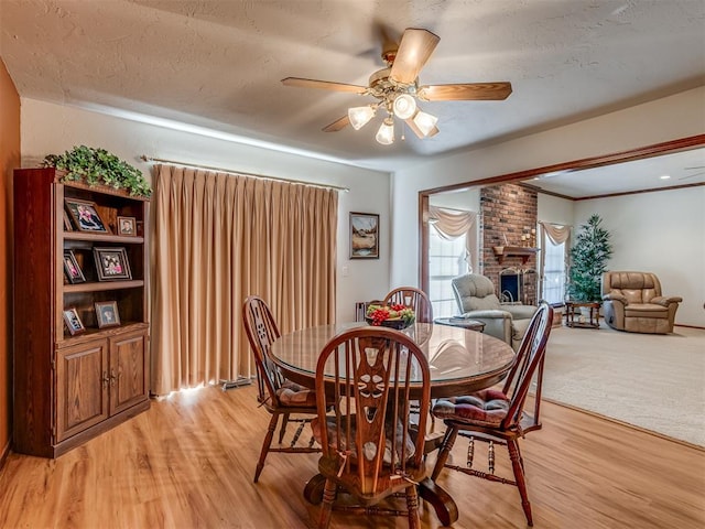 dining space featuring ceiling fan, light hardwood / wood-style floors, a textured ceiling, and a brick fireplace