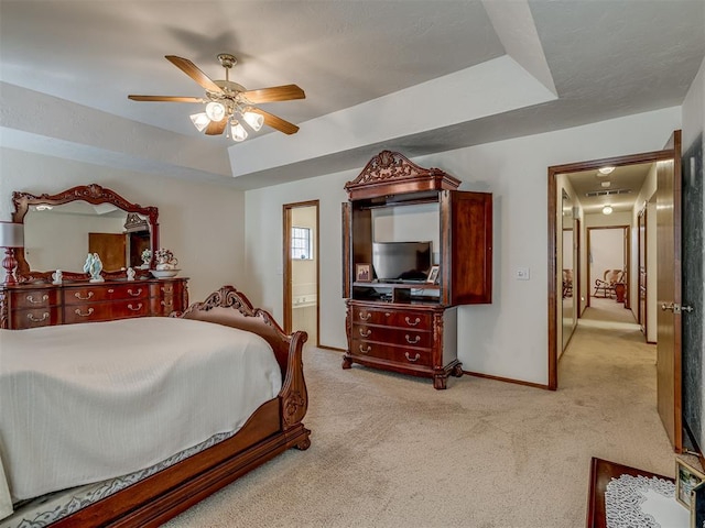 carpeted bedroom featuring ceiling fan, a tray ceiling, and ensuite bath