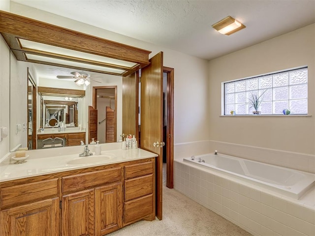 bathroom featuring ceiling fan, vanity, a relaxing tiled tub, and a textured ceiling