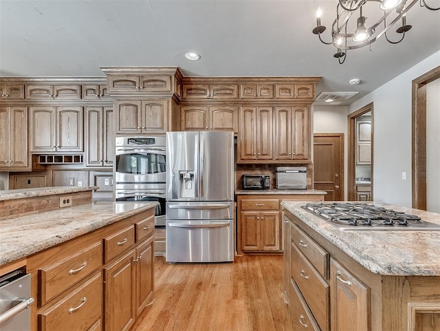 kitchen with pendant lighting, light wood-type flooring, a kitchen island, stainless steel appliances, and a chandelier