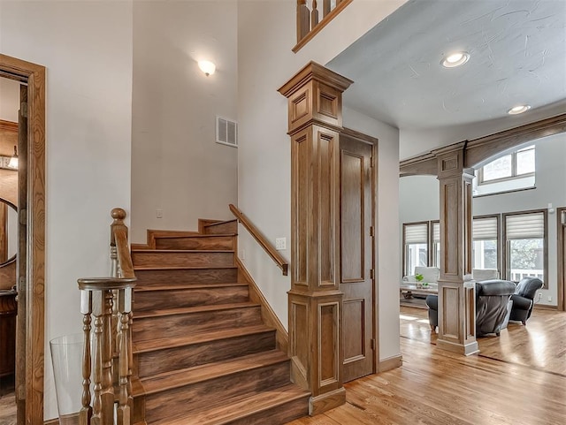 staircase featuring hardwood / wood-style floors, ornate columns, and a high ceiling