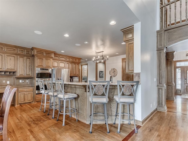 kitchen with appliances with stainless steel finishes, light wood-type flooring, hanging light fixtures, and a notable chandelier