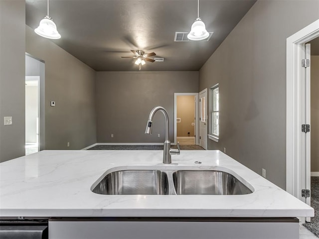 kitchen featuring sink, light stone counters, hanging light fixtures, and a kitchen island with sink