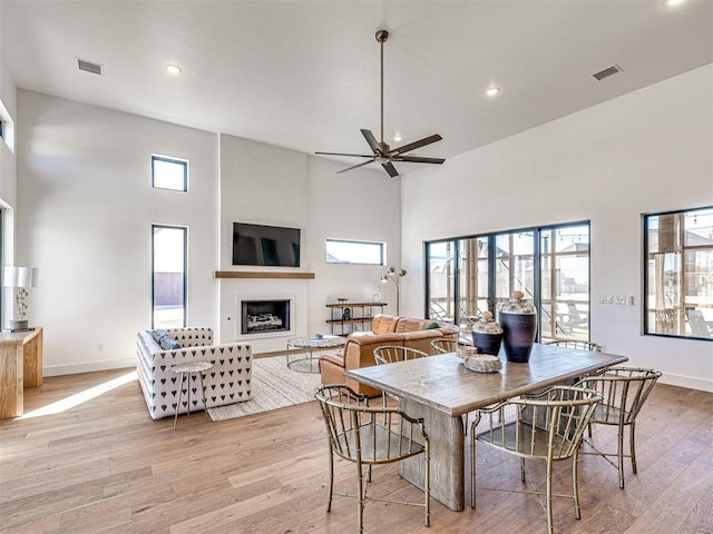 dining room with a towering ceiling, a wealth of natural light, and light hardwood / wood-style flooring