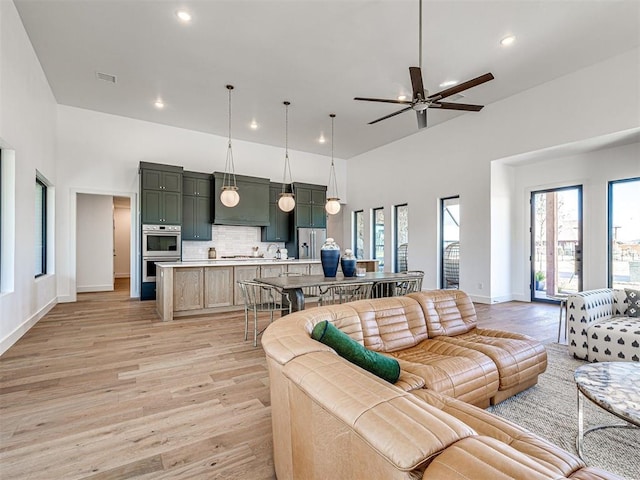 living room featuring ceiling fan, sink, a towering ceiling, and light hardwood / wood-style floors