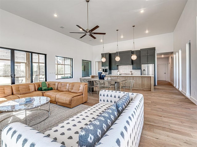 living room featuring ceiling fan, light wood-type flooring, and a high ceiling