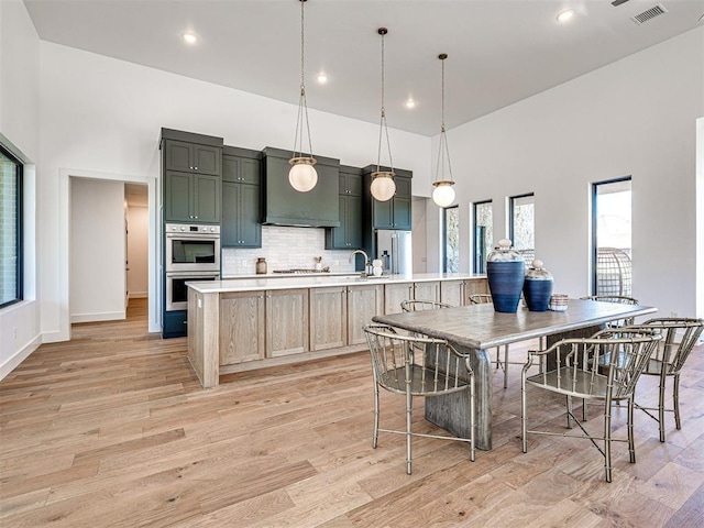 kitchen with hanging light fixtures, light brown cabinetry, a large island, light hardwood / wood-style floors, and stainless steel appliances