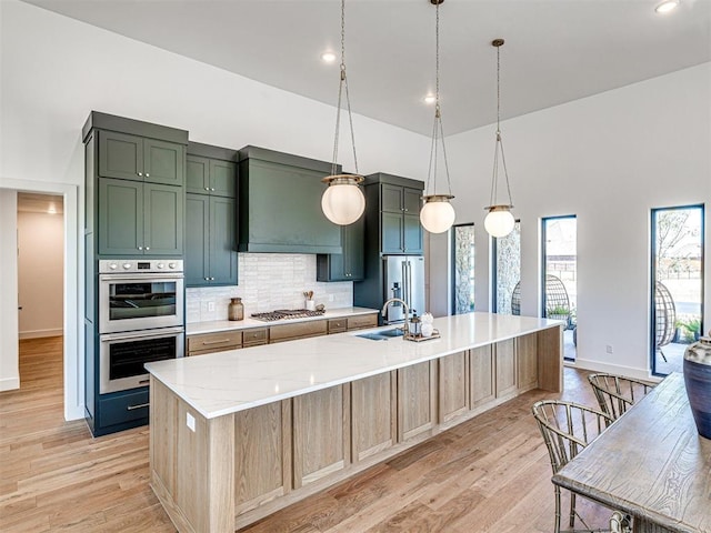 kitchen featuring a center island with sink, hanging light fixtures, light hardwood / wood-style flooring, light stone countertops, and appliances with stainless steel finishes