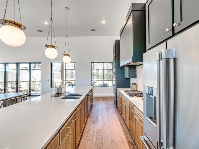 kitchen with appliances with stainless steel finishes, light stone counters, sink, decorative light fixtures, and light hardwood / wood-style flooring