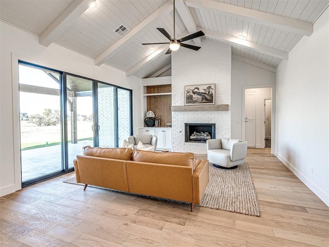 living room featuring vaulted ceiling with beams, ceiling fan, a large fireplace, and light hardwood / wood-style floors