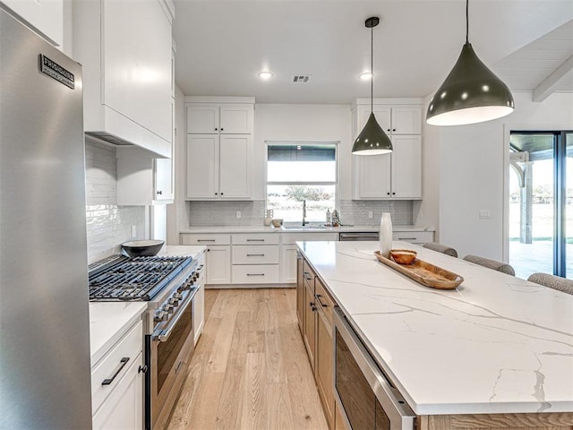 kitchen featuring appliances with stainless steel finishes, light stone counters, light hardwood / wood-style flooring, white cabinets, and a center island