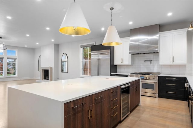 kitchen featuring white cabinetry, wall chimney exhaust hood, pendant lighting, and premium appliances