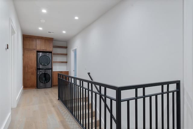 hallway with light wood-type flooring and stacked washing maching and dryer