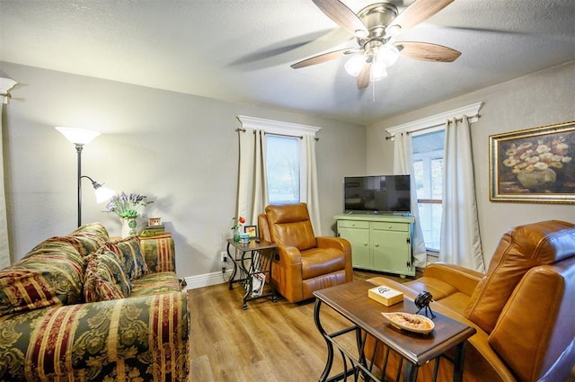 living room featuring a textured ceiling, light wood-style flooring, baseboards, and a ceiling fan