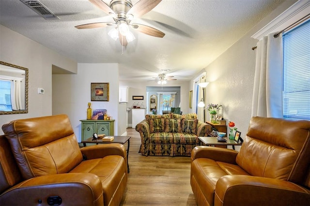 living room featuring a textured ceiling, ceiling fan, visible vents, and wood finished floors