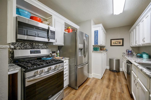 kitchen featuring a textured ceiling, light wood-style flooring, appliances with stainless steel finishes, white cabinetry, and open shelves