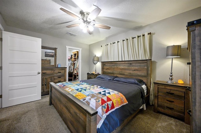carpeted bedroom featuring a closet, a textured ceiling, visible vents, ceiling fan, and a walk in closet
