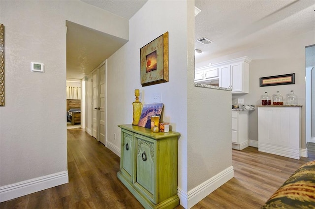 hallway with baseboards, visible vents, wood finished floors, and a textured ceiling