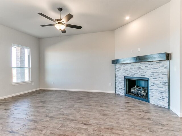 unfurnished living room with a stone fireplace, ceiling fan, and light hardwood / wood-style floors