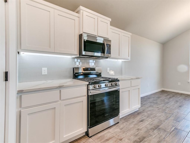 kitchen featuring decorative backsplash, appliances with stainless steel finishes, light wood-type flooring, light stone counters, and white cabinetry