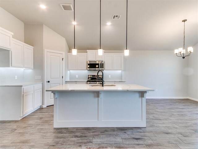 kitchen featuring lofted ceiling, decorative light fixtures, a kitchen island with sink, white cabinets, and appliances with stainless steel finishes