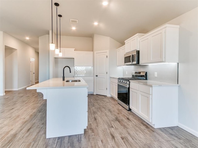 kitchen with sink, stainless steel appliances, light hardwood / wood-style flooring, an island with sink, and pendant lighting