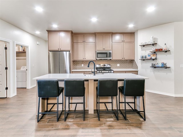 kitchen with a center island with sink, washer / dryer, stainless steel appliances, and hardwood / wood-style flooring