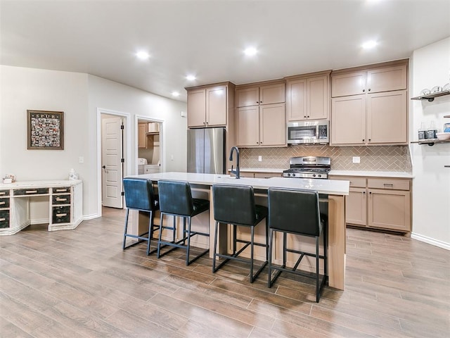 kitchen with a center island with sink, a breakfast bar area, light hardwood / wood-style flooring, washer and dryer, and stainless steel appliances