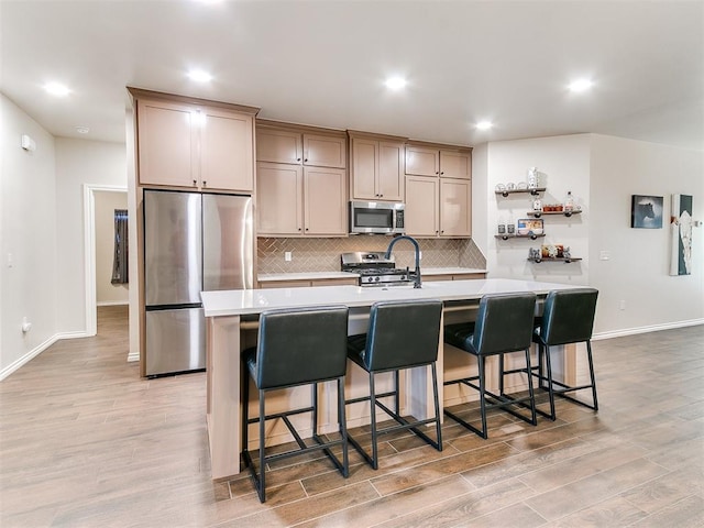 kitchen with stainless steel appliances, a kitchen breakfast bar, light hardwood / wood-style flooring, an island with sink, and light brown cabinetry