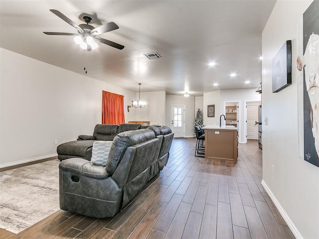 living room with ceiling fan with notable chandelier, sink, and dark wood-type flooring