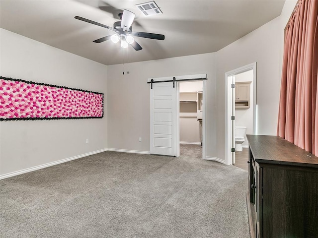 unfurnished bedroom with carpet flooring, a walk in closet, ensuite bathroom, ceiling fan, and a barn door