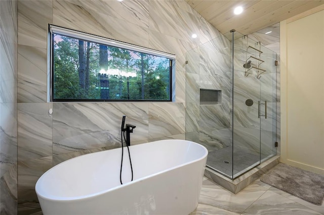 bathroom featuring plus walk in shower and tile walls