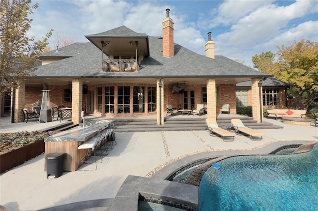 rear view of house with a swimming pool with hot tub, a patio area, and a balcony