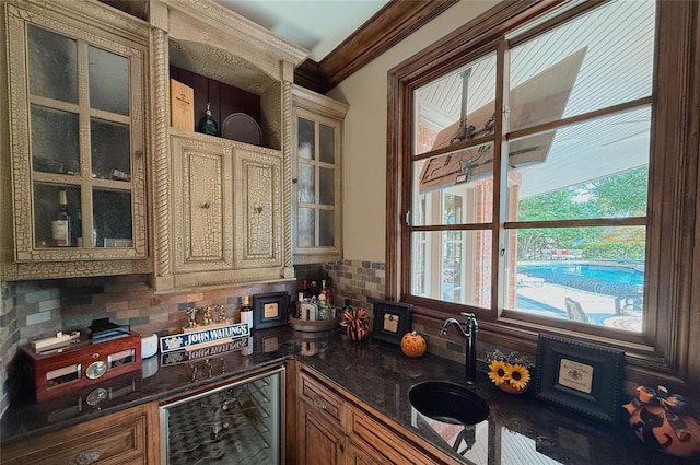 kitchen featuring sink, beverage cooler, backsplash, dark stone countertops, and ornamental molding