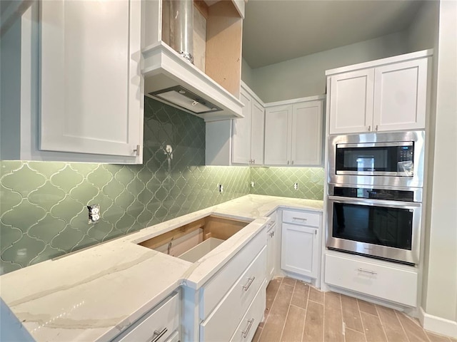 kitchen with white cabinets, light hardwood / wood-style floors, light stone counters, and wall chimney exhaust hood