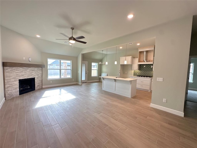 unfurnished living room featuring vaulted ceiling, light hardwood / wood-style floors, a stone fireplace, and ceiling fan