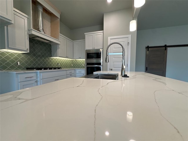 kitchen featuring white cabinets, a barn door, light stone counters, and appliances with stainless steel finishes