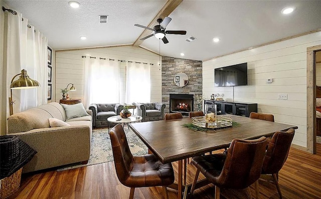 living room featuring lofted ceiling with beams, a stone fireplace, ceiling fan, a textured ceiling, and dark hardwood / wood-style flooring