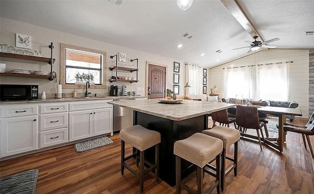 kitchen with white cabinets, sink, vaulted ceiling, stainless steel dishwasher, and a kitchen island