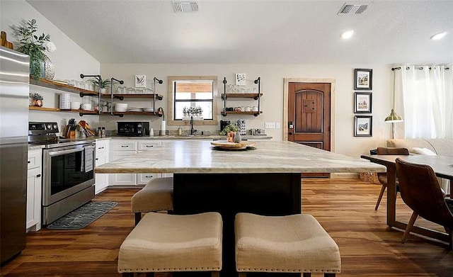 kitchen featuring a center island, dark hardwood / wood-style flooring, a breakfast bar, white cabinets, and appliances with stainless steel finishes