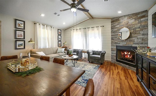 living room with wood-type flooring, vaulted ceiling with beams, a stone fireplace, and ceiling fan