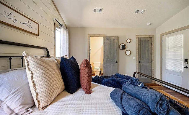 bedroom with hardwood / wood-style floors, ensuite bathroom, multiple windows, and lofted ceiling