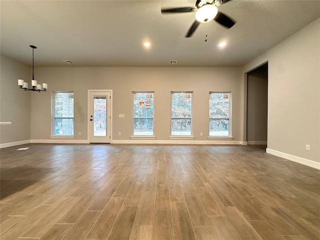 unfurnished living room with ceiling fan with notable chandelier and wood-type flooring