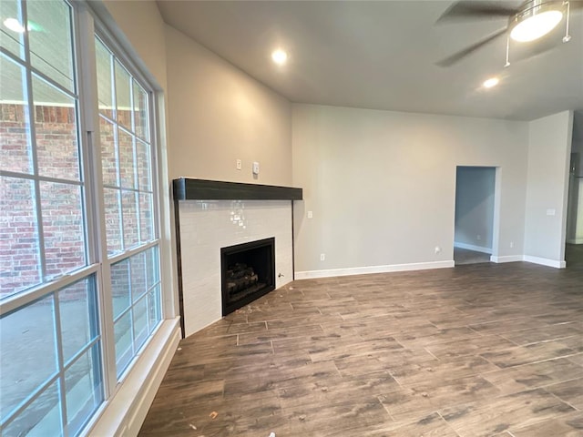 unfurnished living room featuring a tiled fireplace, ceiling fan, and wood-type flooring