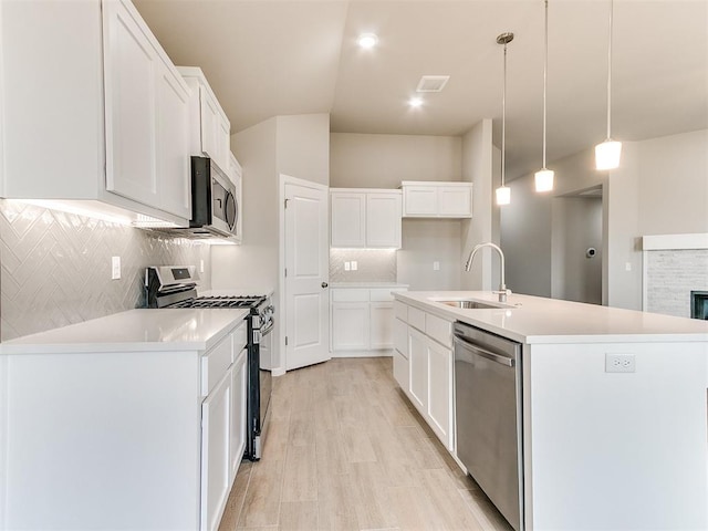 kitchen featuring a center island with sink, sink, decorative light fixtures, white cabinetry, and stainless steel appliances