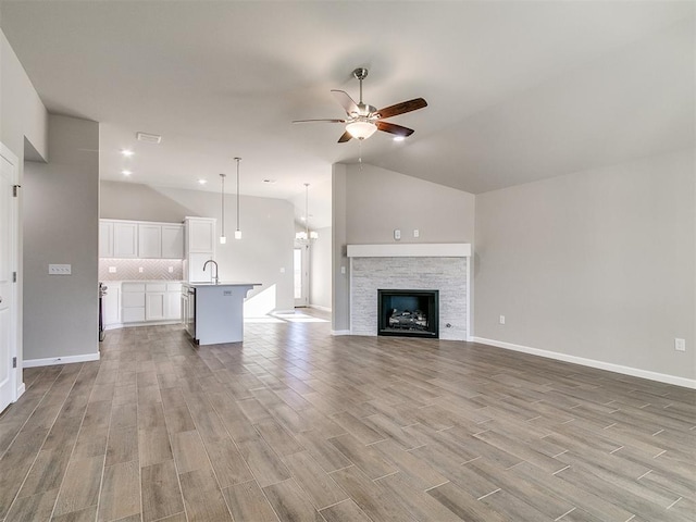 unfurnished living room featuring vaulted ceiling, ceiling fan, a stone fireplace, and sink