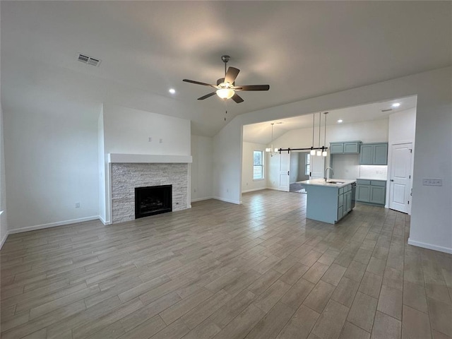 unfurnished living room with sink, light hardwood / wood-style floors, vaulted ceiling, a fireplace, and ceiling fan with notable chandelier