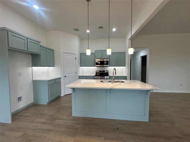 kitchen featuring stainless steel appliances, sink, wood-type flooring, decorative light fixtures, and an island with sink