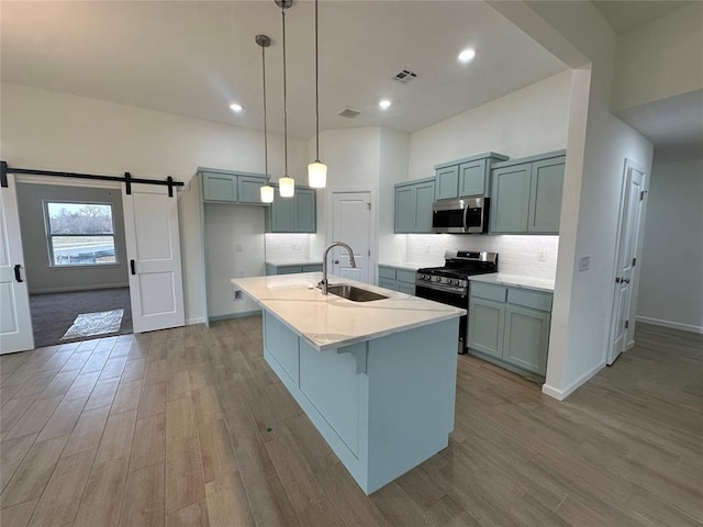 kitchen featuring stainless steel appliances, sink, a barn door, a center island with sink, and light hardwood / wood-style floors